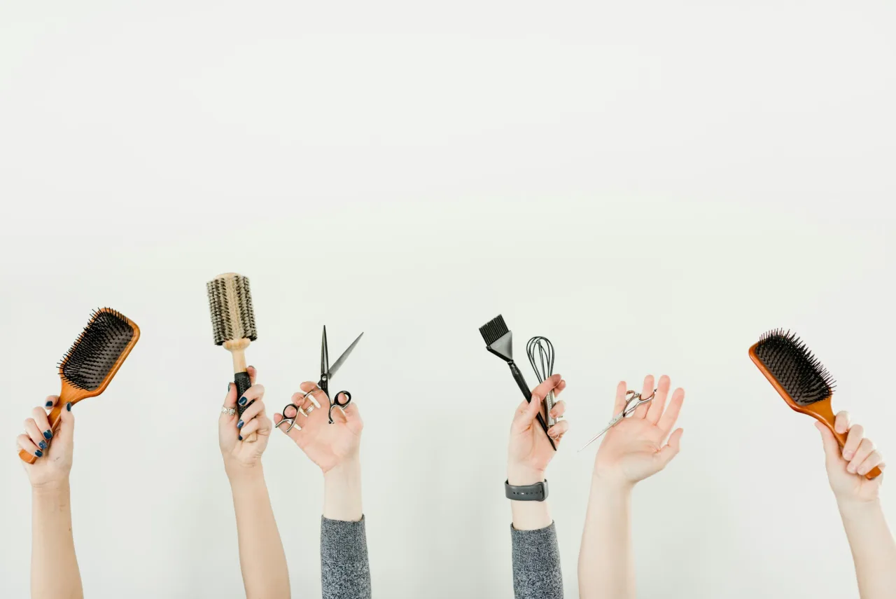 Mani che sollevano gli strumenti del mestiere: spazzole, forbici e pettini