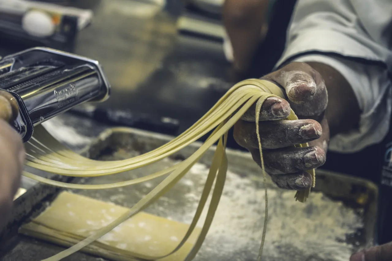 Lavorazione a mano di tagliatelle fresche con farina e macchina per la pasta
